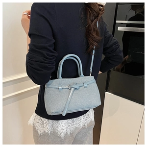 Close-up of light blue twill handbag with decorative buckle and detachable strap