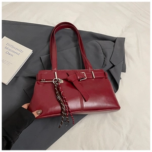 Detail of burgundy leather shoulder bag with decorative buckle and woven rope keychain