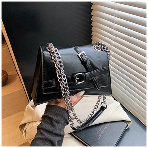 Detail of black glossy trapezoid chain bag with parallel buckle straps and silver chain