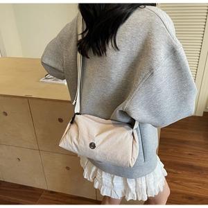 Detail of beige nylon crossbody bag featuring a round metal logo and adjustable strap