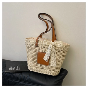 Detail of straw tote bag showing beige woven texture, brown leather patch and lace bow
