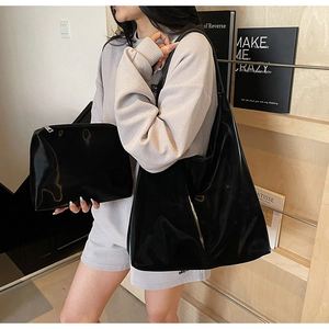 Detail of a black patent leather tote bag set with a matching pouch worn by a model