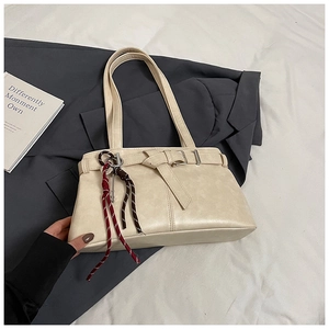 Detail view of beige faux leather shoulder bag with strap buckle and braided charms