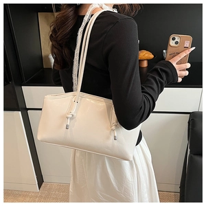 Detail of a minimalist off-white leather tote bag with knotted shoulder straps and silver accents