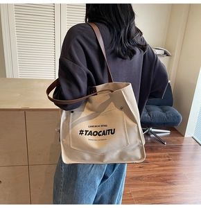 Detail of off-white canvas tote with brown leather strap and front pocket on model