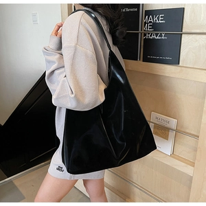 Close-up of a large black glossy single shoulder bag with a stylish wide strap