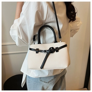 Detail of a beige bucket bag with black handles on a model in a minimal indoor setting