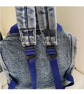 Detail view of adjustable woven strap and black plastic buckle on washed denim backpack