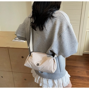 Rear view of a model wearing a minimalist beige nylon crossbody bag with wide shoulder strap