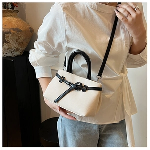 Detail of off-white woven texture bucket bag with black leather handle and knot strap