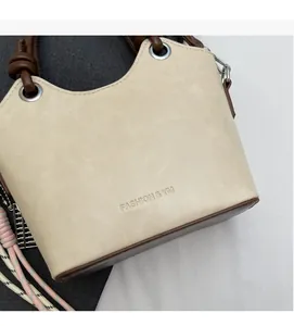 Détail du sac seau crème avec logo gaufré et poignée marron à nœuds élégants