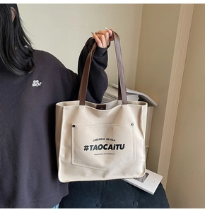 Detail of canvas tote bag with brown straps and large front pocket featuring black text