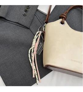 Détail du sac seau beige avec charm en corde tressée rose sur un blazer gris en fond