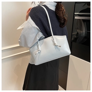 Detail of glossy light blue tote bag showing the metal knot buckle and smooth PU leather