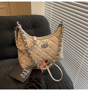 Detail einer gesteppten beige Handtasche mit silberner Kette und quadratischem Drehverschluss
