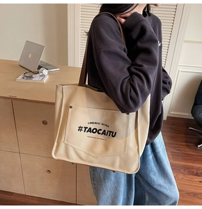Close-up of beige canvas tote bag with brown straps and large front lettered pocket