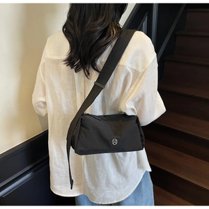 Detail of a black nylon crossbody bag with wide strap and circular metal logo on white shirt