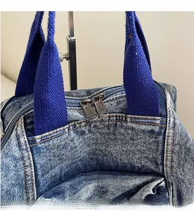 Detail of smooth metal double zippers and blue woven handles on washed denim backpack
