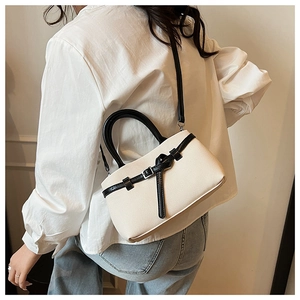 Detailed side view of beige bucket bag with black handle worn by model for scale