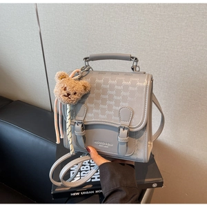 Détail d'un sac à main gris avec motif texturé, logo gravé et petit porte-clé ours