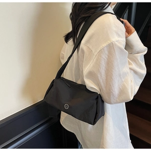 Detail of minimalist black nylon crossbody bag with silver M logo and wide shoulder strap