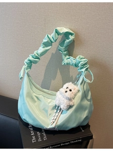 Mint green nylon hobo bag with pleated strap and plush dog charm on a book