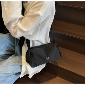 Detail of black nylon crossbody pillow bag with metal M logo and wide woven strap