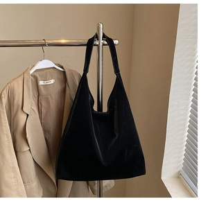 Chic black velvet hobo tote bag hanging with a khaki trench coat in a cozy setting