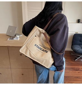 Detail view of large canvas tote bag with brown straps and contrast front pocket for commuting