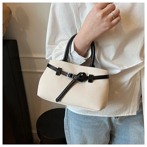 Detailed shot of beige woven bucket bag featuring black leather handles and buckle strap