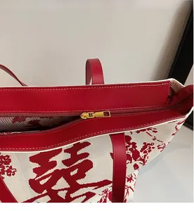 Detail view of the smooth golden metal zipper and red leather trim on the tote bag