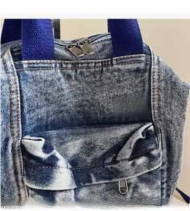 Detail of dark blue washed denim backpack with metal zippers and orange contrast stitching