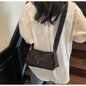 Detail of minimalist black nylon crossbody bag with metal logo on model in urban setting