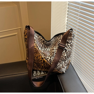 Detail of leopard print tote bag featuring a wide adjustable fabric strap on a leather sofa