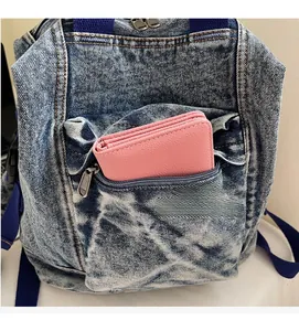 Close-up of front zipper pocket on washed denim backpack showing storage capacity