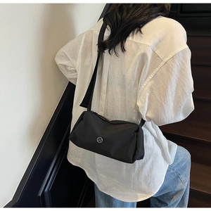 Detail of a black nylon crossbody pillow bag with silver round logo on stairs background