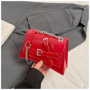 Detail of red patent leather crossbody bag featuring silver chain strap and buckle accents
