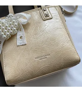 Gros plan sur la texture cuir plissé beige et le charme nœud dentelle perle