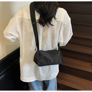 Detail of black nylon crossbody bag featuring wide strap and round metal logo on model