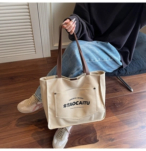 Detail of beige canvas tote bag featuring brown leather straps and black printed text logo