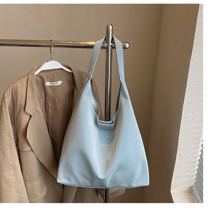 Detail of light blue leather tote bag showing a minimalist triangular silhouette on a hanger