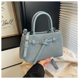 Detail view of light blue denim bucket bag with metal buckle strap and woven texture