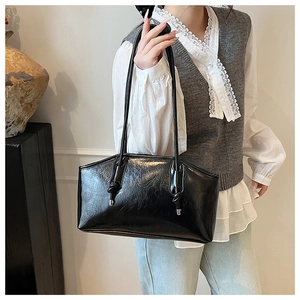 Detail of glossy black leather underarm bag with unique knotted strap and metal hardware
