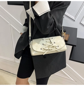 Close-up of a cream corset-style baguette bag with lace-up detail and glossy leather