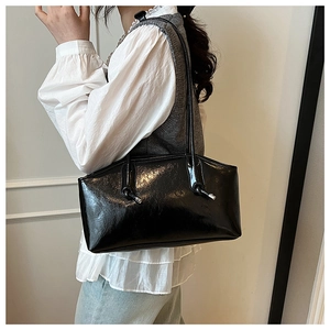 Close-up of black glossy oil wax leather tote bag featuring elegant knotted shoulder straps