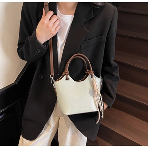 Détail du sac seau vert clair avec poignées marron, pompons et pendentif de tennis