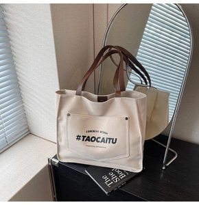 Detail of off-white canvas tote bag with brown handles and front pocket lettering