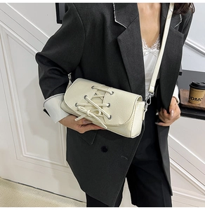 Detail of cream white shoulder bag featuring criss-cross straps and bow decoration on flap