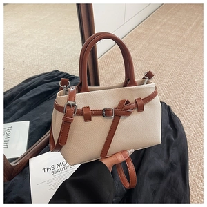 Detail of beige canvas bucket bag with brown leather handles and metal buckle accents
