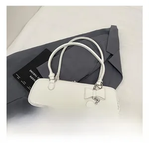 Detail of white baguette bag featuring a 3D bow and a heart charm on a grey suit